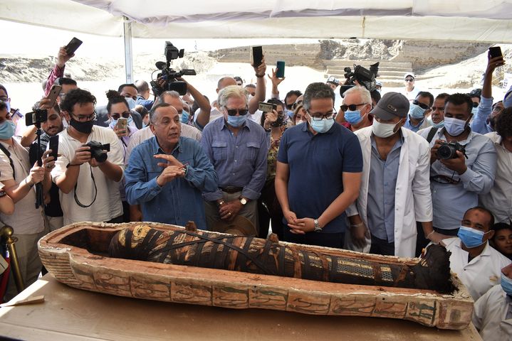 Mostafa Waziri, secrétaire général du Conseil suprême des Antiquités (à gauche) et Khaled el-Enani, ministre du Tourisme et des Antiquiés (tee-shirt et masque), observent la momie intacte d'un sarcophage juste après son ouverture, le 3 octobre 2020 à Saqqara (ZIAD AHMED / NURPHOTO / AFP)