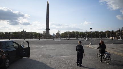 Des policiers vérifient l'attestation de déplacement dérogatoire d'une cycliste sur la place de la Concorde, à Paris, le 18 mars 2020. (NICOLAS PORTNOI / HANS LUCAS / AFP)