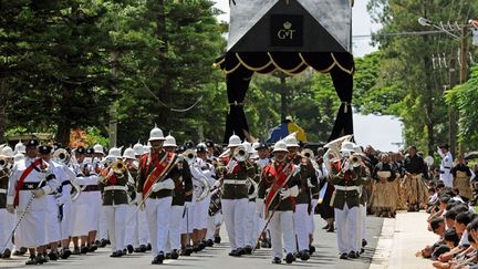 Un orchestre militaire marche en tête du cortège. Des centaines d'habitants sont rassemblés, pour accompagner la procession. (AFP PHOTO / Torsten BLACKWOOD)