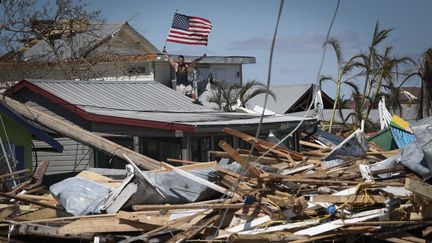 Un habitant de l'île de Matlacha, en Floride (Etats-Unis), brandit le drapeau américain depuis les décombres de sa maison, le 30 septembre, deux jours après le passage de l'ouragan Ian. (WIN MCNAMEE / GETTY IMAGES NORTH AMERICA / AFP)