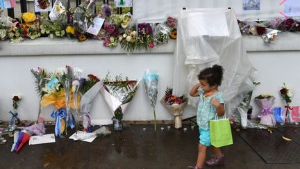 Une petite fille passe devant la façade de l'ambassade de France fleurie et couverte de messages en hommage aux victimes des attentats de Paris. (Roslan RAHMAN / AFP)