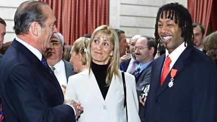 Jacques Chirac remet la L&eacute;gion d'honneur au capitaine des Bleus, Jackson Richardson, apr&egrave;s le titre mondial de 2001. Lors de leur premi&egrave;re rencontre en 1995, le chef de l'Etat s'&eacute;tait adress&eacute; au joueur en anglais, pensant qu'il &eacute;tait naturalis&eacute; et ne parlait pas fran&ccedil;ais. (GEORGES GOBET / AFP)