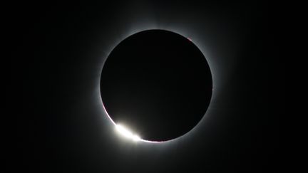 Sur cette image de l'eclipse totale, pris à Madras (Oregon) le 21 août 2017, on peut observer l'effet du "diamant" : comme pour les "perles de Bailly", la lumière passe à travers les reliefs de la Lune, mais en un seul point. (STAN HONDA / AFP)