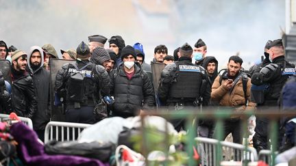 Des migrants réunis près des gendarmes pendant l'évacuation du camp de Grande-Synthe le 16 novembre 2021. (DENIS CHARLET / AFP)