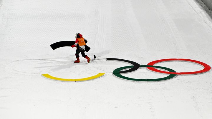 Un volontaire enlève les anneaux olympiques de la piste après l'épreuve de saut à skis des Jeux de Pékin, le 5 février 2022. (CHRISTOF STACHE / AFP)