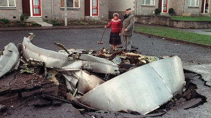 Des habitants de Lockerbie se tiennent près d'un des moteurs de l'avion qui s'est écrasé dans le village écossais, le 22 décembre 1988. (ROY LETKEY / AFP)