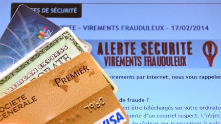 Des cartes bancaires face à un écran d'ordinateur où est inscrit une mise en garde. (DENIS CHARLET / AFP)