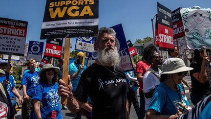 Un membre de la Screen Actors Guild (SAG-AFTRA, syndicat des acteurs), au premier plan, soutient les grévistes de la Writers Guild of America (WGA, syndicat des scénaristes), lors d'une marche en prélude à un rassemblement à La Brea Tar Pits, à Los Angeles (Californie), aux Etats-Unis. (IRFAN KHAN / LOS ANGELES TIMES)