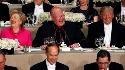 Hillary Clinton et Donald Trump, assis chacun d'un côté du cardinal de New York (nord-est) Timothy Dolan, lors&nbsp;d'un gala de charité&nbsp;jeudi 20 octobre. (ONATHAN ERNST / REUTERS)