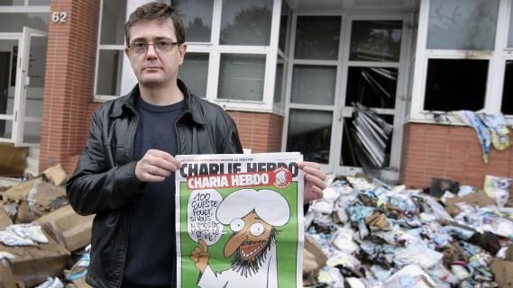 Charb, le directeur de la publication de "Charlie Hebdo", montre la une de l'hebdomadaire satirique devant le si&egrave;ge ravag&eacute; par un incendie &agrave; Paris, le 2 novembre 2011. ((ALEXANDER KLEIN / AFP))