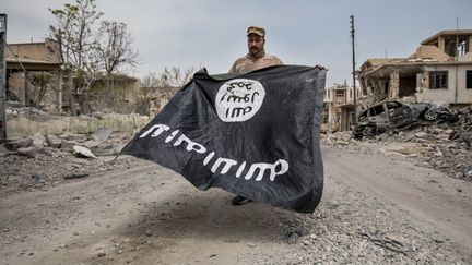 Un drapeau du groupe Etat islamique, exhibé dans les ruines de Mossoul (Irak) par un soldat irakien, le 7 juillet 2017. (SEBASTIAN BACKHAUS / NURPHOTO / AFP)