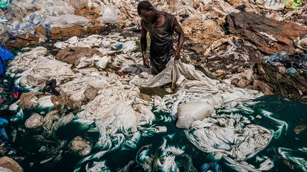 Katabi, Ouganda. Dans une décharge située dans un marécage, un homme nettoie des sacs plastiques dont le colorant bleu va contaminer l’eau du lac Victoria. En s’établissant pour des raisons économiques dans une zone humide, filtre naturel des eaux de ruissellement, les oubliés de la croissance ougandaise la détruisent et contribuent à la pollution du lac. (FREDERIC NOY)