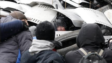 Une polici&egrave;re anti-&eacute;meutes regarde en direction du photographe qui la prend en photo, cach&eacute;e sous des boucliers. (VASILY FEDOSENKO / REUTERS)