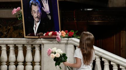 Un fillette dépose des fleurs devant une photo de Johnny Hallyday, à l'église de la Madeleine à Paris, le 15 juin 2018. (PHILIPPE LOPEZ / AFP)