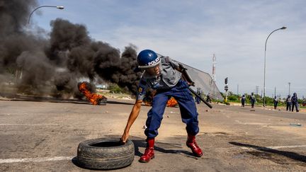 Un policier dégage un pneu de la chaussée, lors d'émeutes à Bulawayo au Zimbabwe, le 14 janvier 2019. (ZINYANGE AUNTONY / AFP)