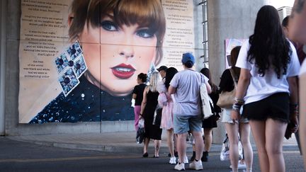 Des "Swifties" font la queue pour un concert de Taylor Swift, devant un mur représentant la chanteuse, le 16 août 2024 à Londres (Royaume-Uni). (JAMES MANNING / MAXPPP)