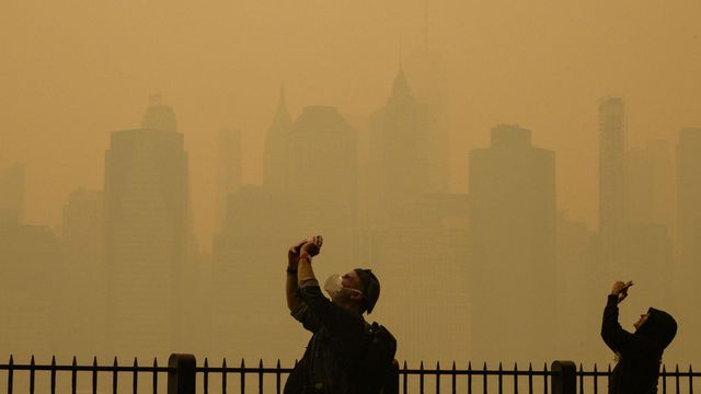 Des passants prennent des photos de cette scène à la beauté inquiétante, en face des gratte-ciels de Manhattan, le 7 juin 2023. (ANGELA WEISS / AFP)