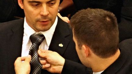 Un membre du parti Jobbik aide son leader, Vona Gabor, au parlement de Budapest. 

"Nous devons rendre le pays au peuple hongrois, la terre, les produits, la devise et la nation de ce pays seront les propriétés du peuple magyar et non pas celles de l'UE, d'Israël ou de Washington", déclare son président, Gabor Vona. (AFP PHOTO / BALINT PORNECZI )