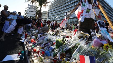 Des passants déposent des bouquets de fleurs, des bougies et des messages, le 16 juillet 2016, sur le mémorial improvisé en hommage aux victimes de l'attentat au camion perpétré sur la promenade des Anglais à Nice lors du 14-Juillet. (VALERY HACHE / AFP)