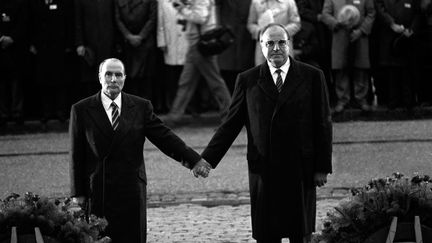 Le président François Mitterrand (G) et le chancelier allemand Helmut Kohl se tiennent la main en écoutant les hymnes nationaux français et allemand lors d'une cérémonie de réconciliation commémorant le souvenir des soldats français et allemands tombés pendant les deux guerres mondiales et scellant l'entente retrouvée, le 22 septembre 1984 à Douaumont, près de Verdun. (MARCEL MOCHET / AFP)