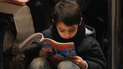 Un enfant lit "Picsou magazine" dans la queue pour l'Eurostar à la gare londonnienne de Saint-Pancras, le 21 décembre 2010.&nbsp; (BEN STANSALL / AFP)
