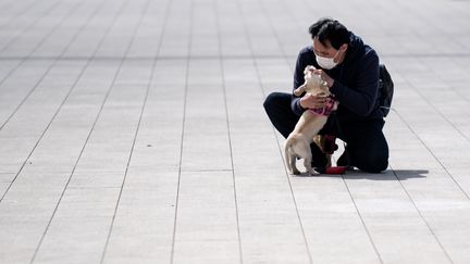 Un homme porte un masque contre le coronavirus Covid-19 et enlasse son chien, à Tokyo le 12 mars 2020. (PHILIP FONG / AFP)