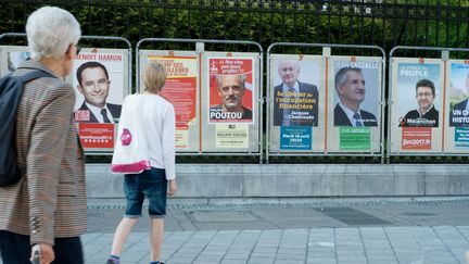 Deux électeurs passent devant les&nbsp;affiches de campagne des candidats à l'élection présidentielle, à Pau (Pyrénées-Atlantiques) le 10 avril 2017. (LAURENT FERRIERE / HANS LUCAS / AFP)