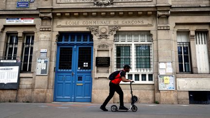 Un adolescent passe en&nbsp;trottinette devant une école élémentaire fermée pour cause de confinement, à Paris le 24 avril 2020. (THOMAS COEX / AFP)