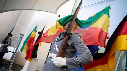 Le drapeau éthiopien recouvre le visage d'un soldat de la Bundeswehr montant la garde devant la chancellerie fédérale d'Allemagne qui accueille le sommet «Compact with Africa». Dans ce cadre, le Ghana, la Tunisie et la Côte d'Ivoire ont déjà reçu 365 millions d'euros d'aides financières sous forme principalement de prêts bonifiés. Les géants industriels allemands Siemens et Volkswagen parrainent notamment cette initiative, laquelle a été créée lors de la présidence allemande du G20 en 2017 et à laquelle participent douze pays africains. Dans la pratique, le nouveau fonds d'un milliard d'euros octroyé au continent servira à garantir des prêts et des fonds propres aux PME européennes et allemandes qui souhaitent investir en Afrique et des fonds propres pour les PME africaines. Plusieurs ONG reprochent toutefois à ce programme de ne pas assez aider les pays les plus pauvres mais ceux qui profitent déjà d'un développement économique. Et de favoriser les entreprises allemandes.

	 

	 

	  (KAY NIETFELD / DPA)