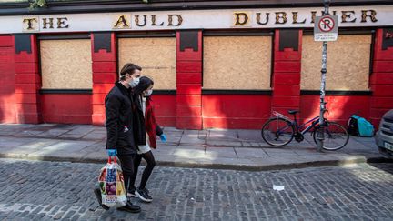 Un couple masqué passe devant un pub fermé à cause du coronavirus, le 25 mars 2020. (PAUL FAITH / AFP)