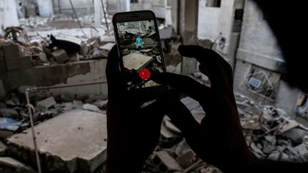 Un homme joue à "Pokémon Go" au milieu des décombres de la ville de Douma (Syrie), située au nord-est de&nbsp;Damas, le 23 juillet 2016. (SAMEER AL-DOUMY / AFP)