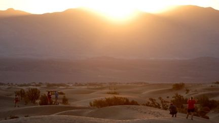 Des visiteurs regardent le lever du soleil sur les dunes de Mesquite Flat, dans le parc national de la vallée de la Mort (Californie), le 9 juillet 2024. (MARIO TAMA / GETTY IMAGES NORTH AMERICA / AFP)