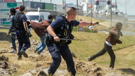 Un policier pulvérisant du gaz lacrymogène sur un migrant, à Calais, tentant de se rendre en Angleterre, le 17 juin 2015. (PHILIPPE HUGUEN / AFP)