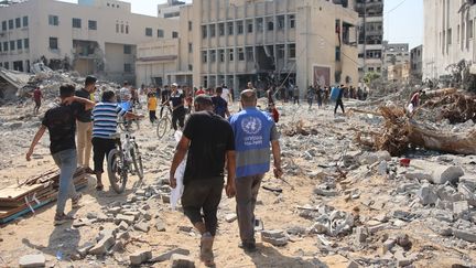 Les gens marchent sur des décombres alors qu’ils inspectent les dégâts au complexe de l’UNRWA dans le quartier d’Al-Sinaa à l’ouest de la ville de Gaza, le 12 juillet, 2024. (OMAR AL-QATTAA / AFP)