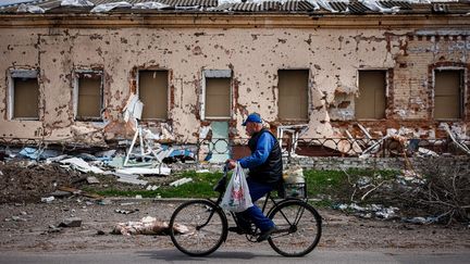 Un homme passe à vélo devant une maison détruite dans le village de Derhachi, au nord de Kharkiv, dans l'est de l'Ukraine, le 27 avril 2022. (DIMITAR DILKOFF / AFP)