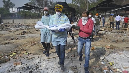 Un homme porte le corps d'un enfant mort du Covid-19, le 12 mai 2021, à New Delhi (Inde). (ARUN SANKAR / AFP)