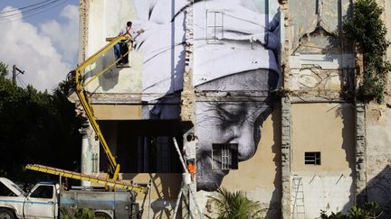 Des ouvriers installent une oeuvre murale r&eacute;alis&eacute;e conjointement par l'artiste am&eacute;ricano-cubain Jose Parla et le Fran&ccedil;ais J.R. sur un immeuble de La Havane (Cuba), le 9 mai 2012. (DESMOND BOYLAN / REUTERS)