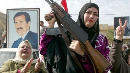 Une femme arbore fièrement une Kalachnikov pendant une manifestation de soutien à Saddam Hussein à Bagdad, en février 2002. Le président irakien est soumis à l'hostilité de George Bush qui le renversera en envahissant le pays en 2003. (AWAD AWAD / AFP)