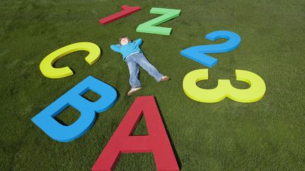 Un enfant couch&eacute; dans l'herbe, entre chiffres et lettres. (LES AND DAVE JACOBS / CULTURA CREATIVE / AFP)