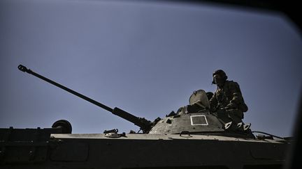 Un membre des troupes ukrainiennes se tient debout sur un véhicule blindé se dirigeant vers la ligne de front dans la ville de Lysychansk, dans la région du Donbas, dans l'est de l'Ukraine, le 9 juin 2022. (ARIS MESSINIS / AFP)