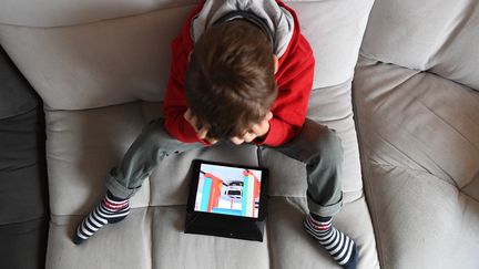 Un enfant regarde un écran assis sur son canapé. Photo d'illustration. (JOSSELIN CLAIR / MAXPPP)