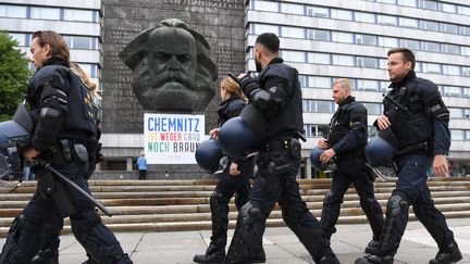 Des policiers marchent devant la statue de Karl-Marx à Chemnitz (Allemagne), le 1er septembre 2018, en marge des deux manifestations&nbsp;de militants d'extrême droite et de gauche. (RALF HIRSCHBERGER / DPA)