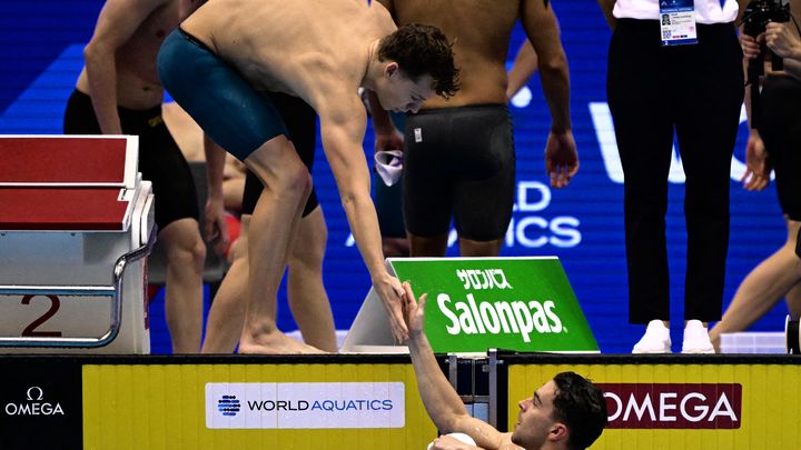 Le nageur français Léon Marchand frappe la main de son collègue du relais 4x100m quatre nages, Hadrien Salvan lors des séries des Mondiaux de natation de Fukuoka, le 30 juillet 2023 (YUICHI YAMAZAKI / AFP)