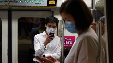 Dans le&nbsp;Mass Rapid Transit train de Singapour, des habitants consultent leur téléphone portable pendant l'épidémie de coronavirus. (CATHERINE LAI / AFP)