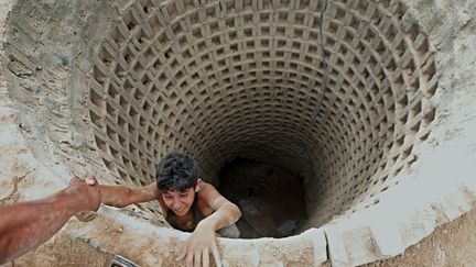 Un Palestinien aide un jeune homme &agrave; sortir d'un tunnel ill&eacute;gal reliant la bande de Gaza &agrave; l'Egypte, le 30 septembre 2012. (SAID KHATIB / AFP)