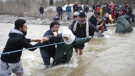 Des migrants tentent de traverser une rivière près de la frontière entre la Grèce et la Macédoine, le 14 mars 2016. (STOYAN NENOV / REUTERS)