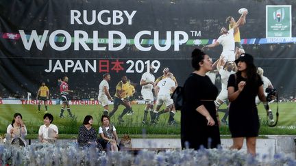 Des Japonaises discutent dans les rues de Kobe (Japon), le 17 septembre 2019, devant un affiche évoquant la Coupe du monde de rugby. (FILIPPO MONTEFORTE / AFP)