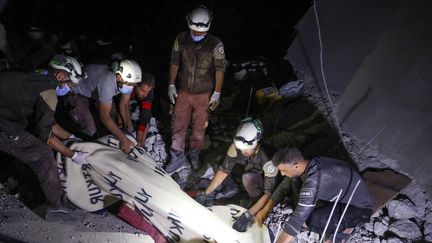 Des membres de la défense civile syrienne extirpent le corps d'une femme des décombres dans le village d'Ehsim (Syrie), le 18 juillet 2021. (OMAR HAJ KADOUR / AFP)