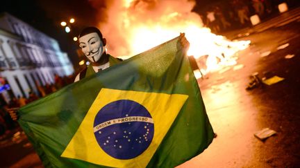 Un manifestant d&eacute;ploie un drapeau br&eacute;silien, lors d'affrontements avec les forces de l'ordre, &agrave; Rio de Janeiro, le 17 juin. (CHRISTOPHE SIMON / AFP)