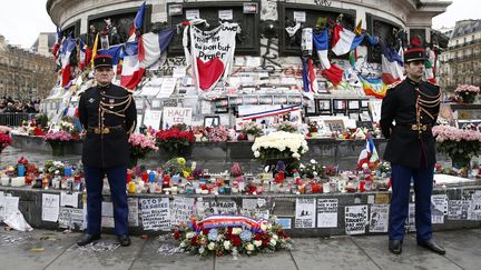 Des gardes républicains se tiennent devant la statue de la République, le 10 janvier 2016, à Paris, où des fleurs et des bougies ont été déposées en mémoire des victimes des attentats de novembre 2015. (YOAN VALAT / AFP)